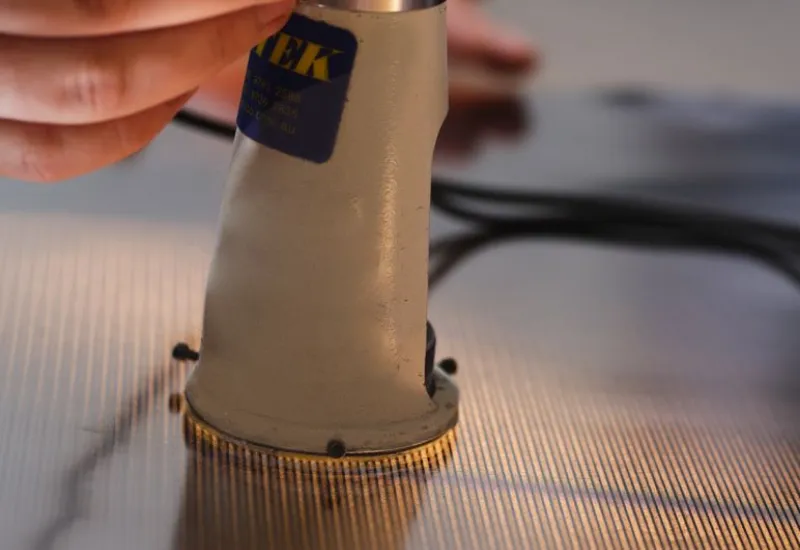 Optical measurement probe inspecting fine metal filtration mesh during a precision quality control process.