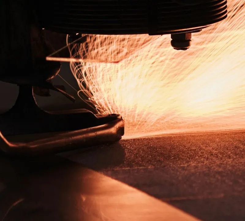 Laser cutting machine cutting a metal sheet with visible sparks during a precision fabrication process.